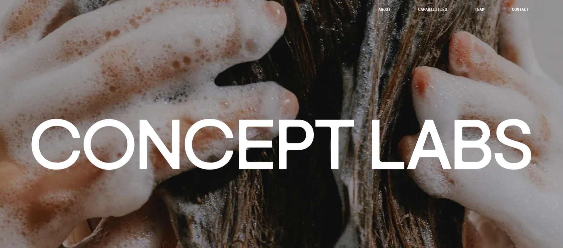 Close-up of hands washing hair with soap bubbles, overlay text reads 'Concept Labs'. Minimal website menu visible in upper corner.